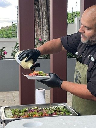 Hombre trabajando en negocio de catering service echando salsa a una ensalada